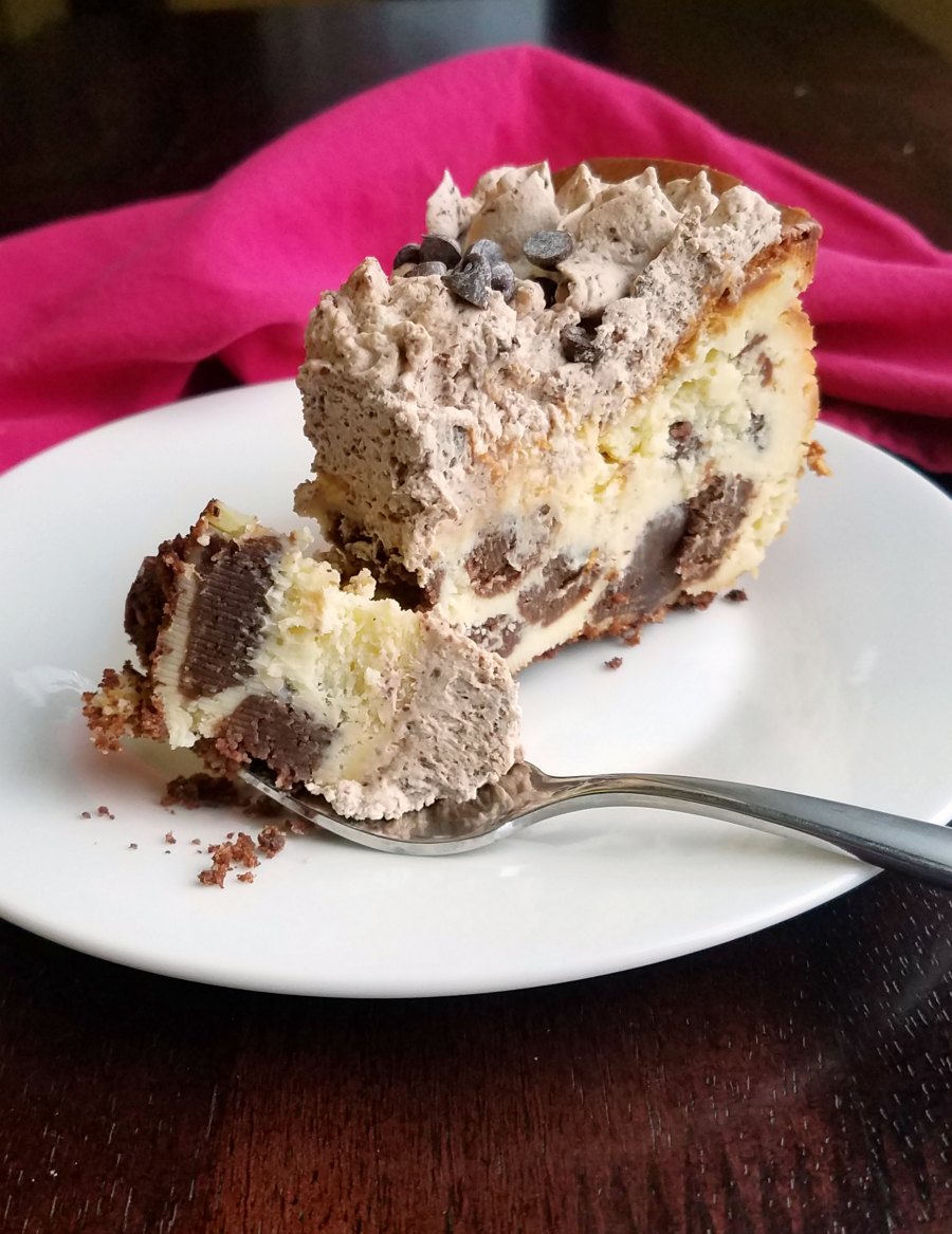 Bite of cheesecake with chunks of brownie baked inside on fork, ready to eat. 