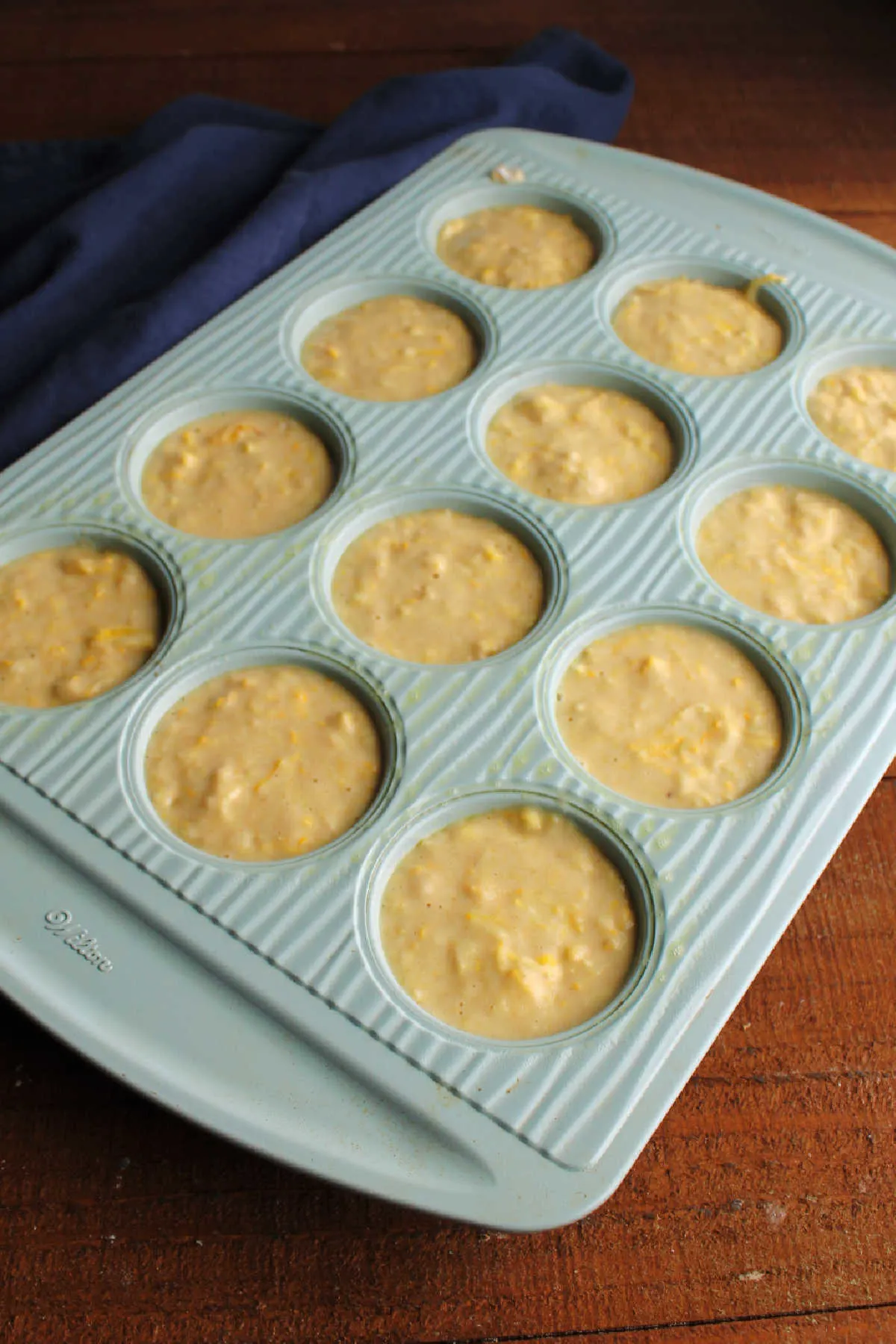 Lemon yellow squash muffin batter spooned into greased muffin pan.