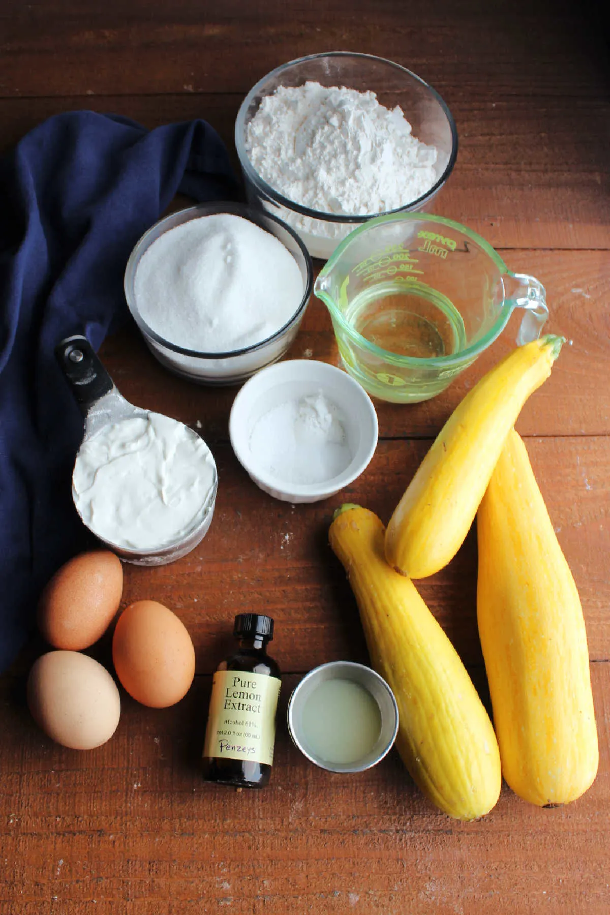 Ingredients including summer squash, lemon juice, lemon extract, eggs, sour cream, oil, sugar, flour, baking powder and salt, ready to be made into muffin batter.