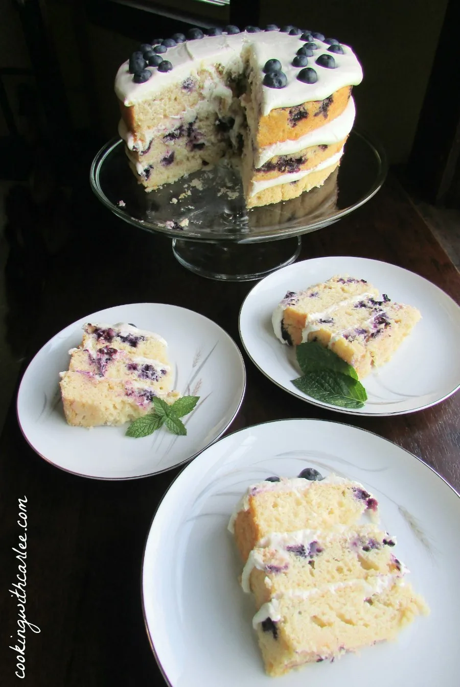 Slices of naked lemon blueberry cake with cream cheese frosting on dessert plates, ready to be served.