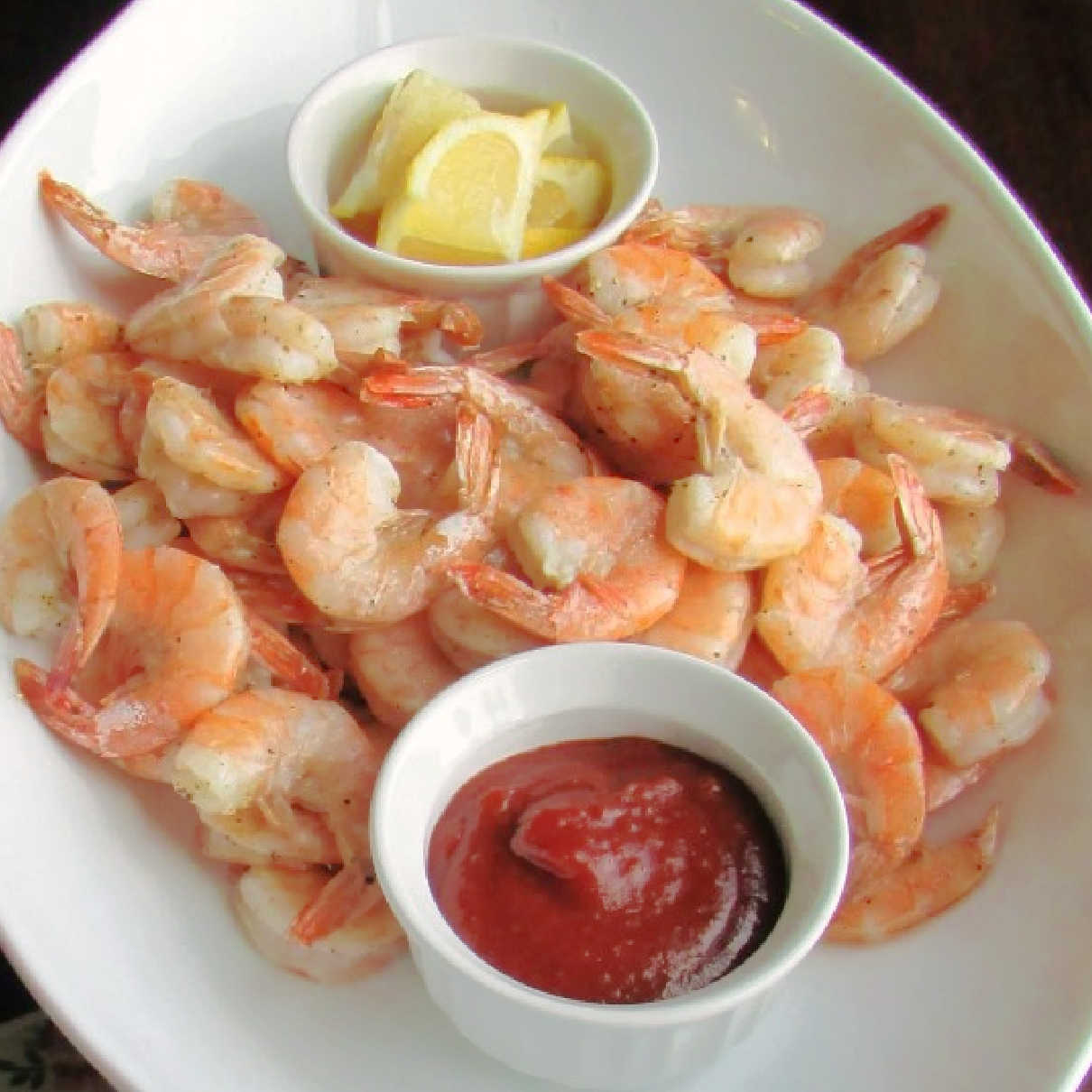 Platter of lemon roasted shrimp with bowl of cocktail sauce and bowl of lemon wedges.