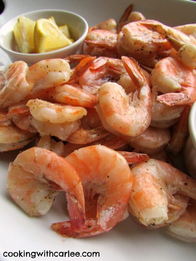 close up of pink roasted shrimp and lemon wedges.