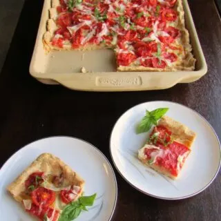 pieces of tomato slab pie in front of tray pan filled with Parmesan cornbread crust, tomatoes and basil.