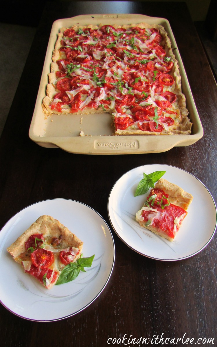 pieces of tomato slab pie in front of tray pan filled with Parmesan cornbread crust, tomatoes and basil.