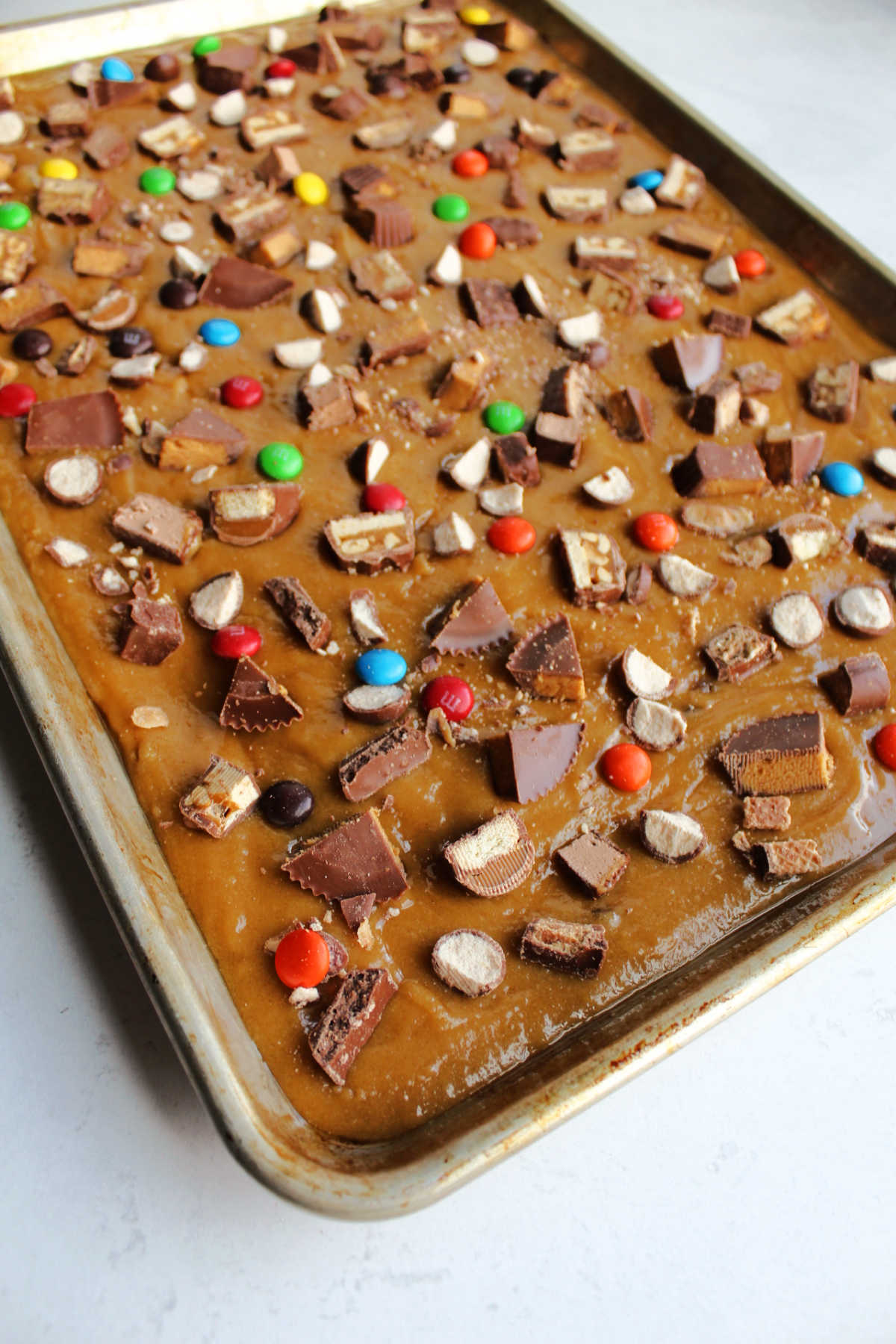 Brown sugar blondie batter in sheet pan with bits of candy bars sprinkled over the top.