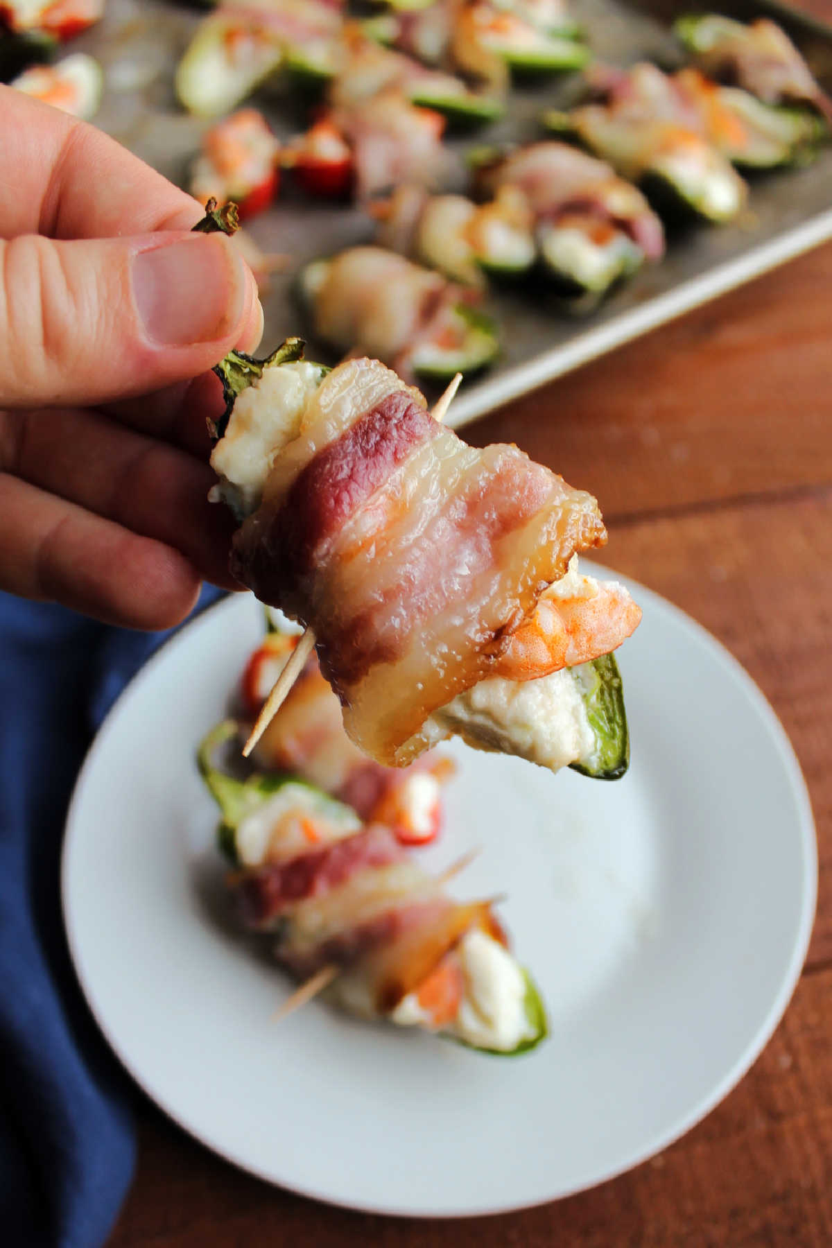 Hand holding jalapeno popper stuffed with garlic cream cheese and a shrimp, wrapped in bacon and cooked.
