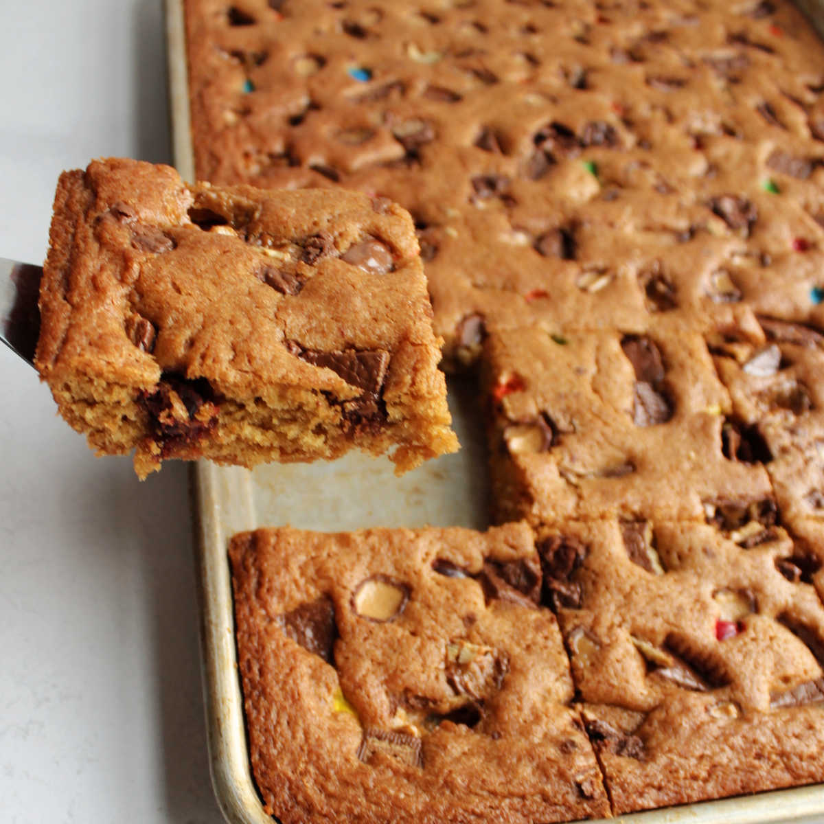 Spatula lifting out piece of candy bar blondies with chewy brown sugar base.