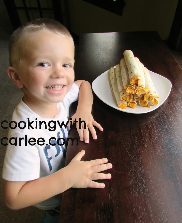 Little Dude smiling proudly next to a stack of buffalo chicken flautas.