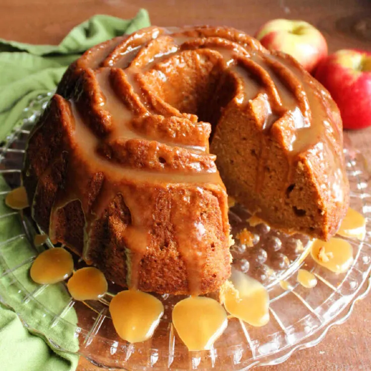 Apple cider bundt cake drizzled with caramel sauce, missing one slice showing moist cake interior.