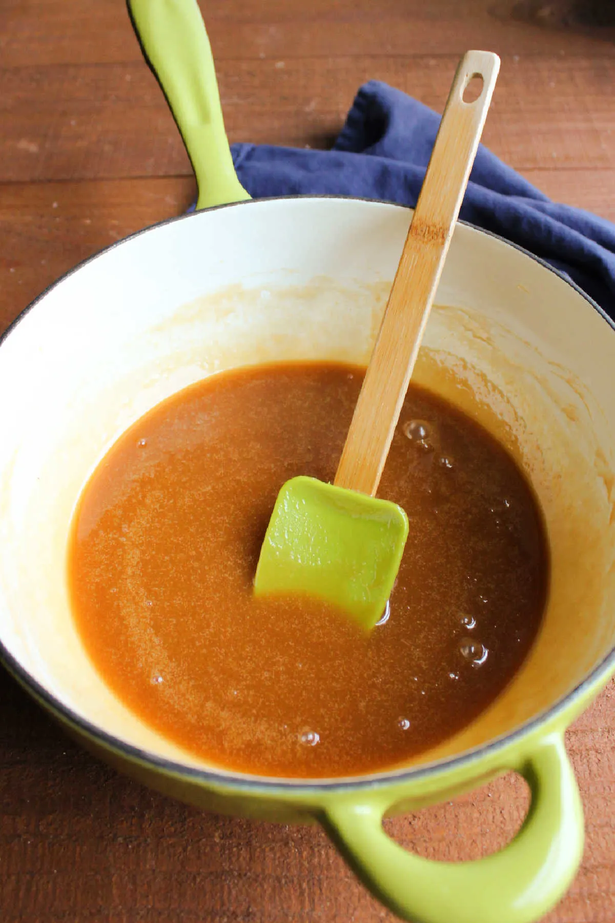 Enameled cast iron saucepan filled with freshly made apple cider caramel sauce and a spatula.