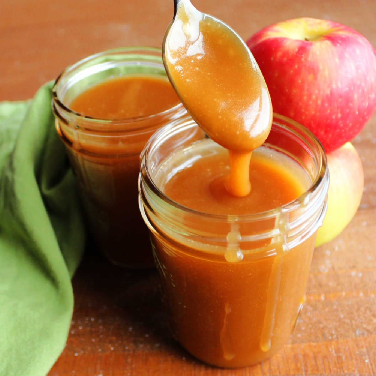 Thick apple cider caramel sauce dripping off a spoon into a jar of more smooth caramel sauce.