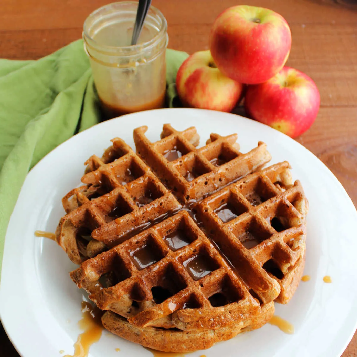 Apple cider belgian waffles drizzled with caramel next to a pile of fresh apples.