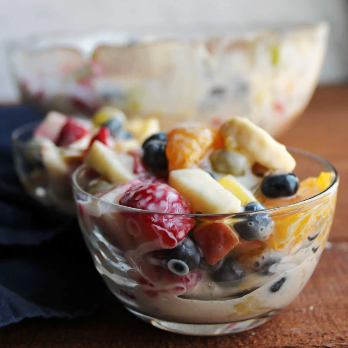 Small glass bowls of fruit salad with fresh berries, bananas, oranges, pineapple, and apples dressed with condensed milk and lemon juice.