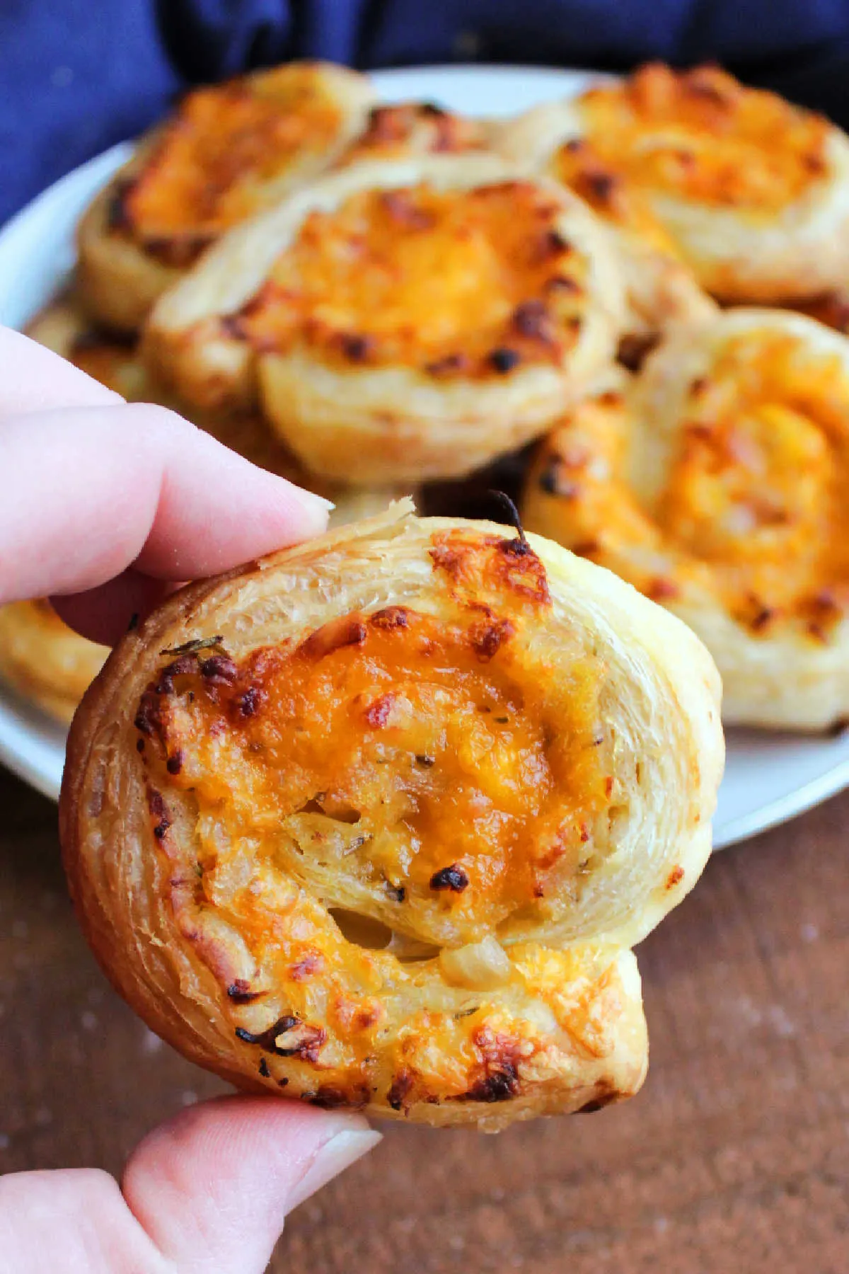 Hand holding apple cheddar puff pastry pinwheel appetizer with golden brown bits of cheese. 