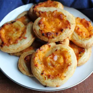 Plate of golden brown puff pastry pinwheels with cheddar, apple and onion filling.