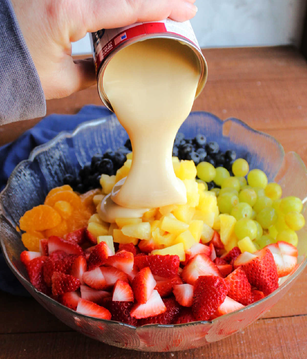 Pouring can of condensed milk over fruit.