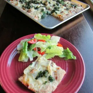 Piece of tuscan pizza on plate with green salad, remaining sheet pan of pizza in background.
