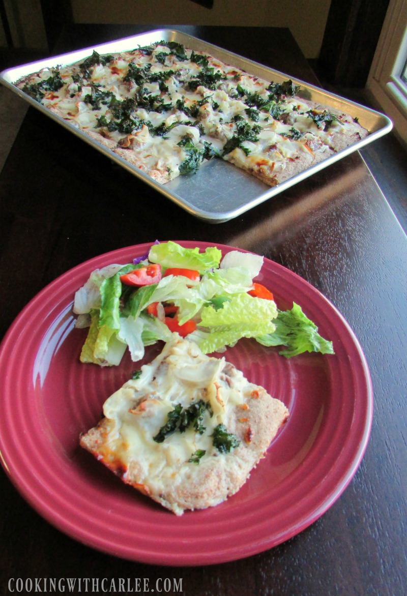 Piece of zuppa toscana pizza on plate with green salad, Remaining sheet pan filled with pizza in background.
