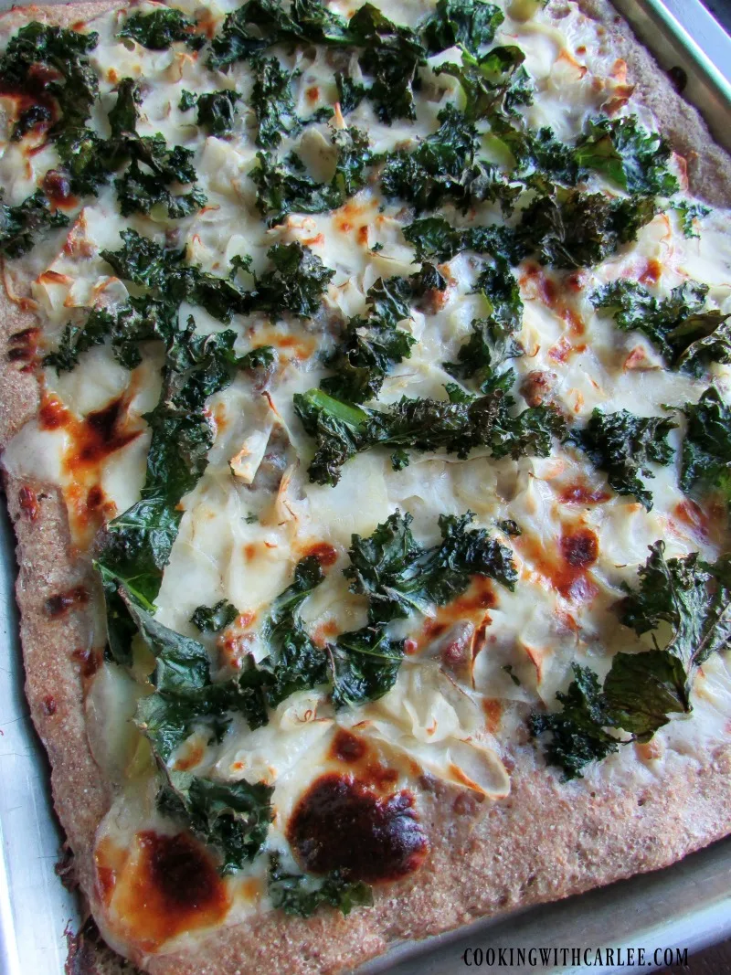 Close up of pizza with golden cheese, kale and potatoes on top.