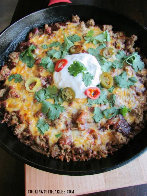 Large cast iron skillet filled with tamale casserole topped with cheese, cilantro, sour cream and jalapenos.