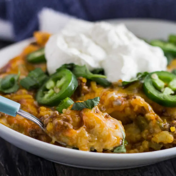 close serving of tamale casserole topped with jalapenos and sour cream, ready to eat.