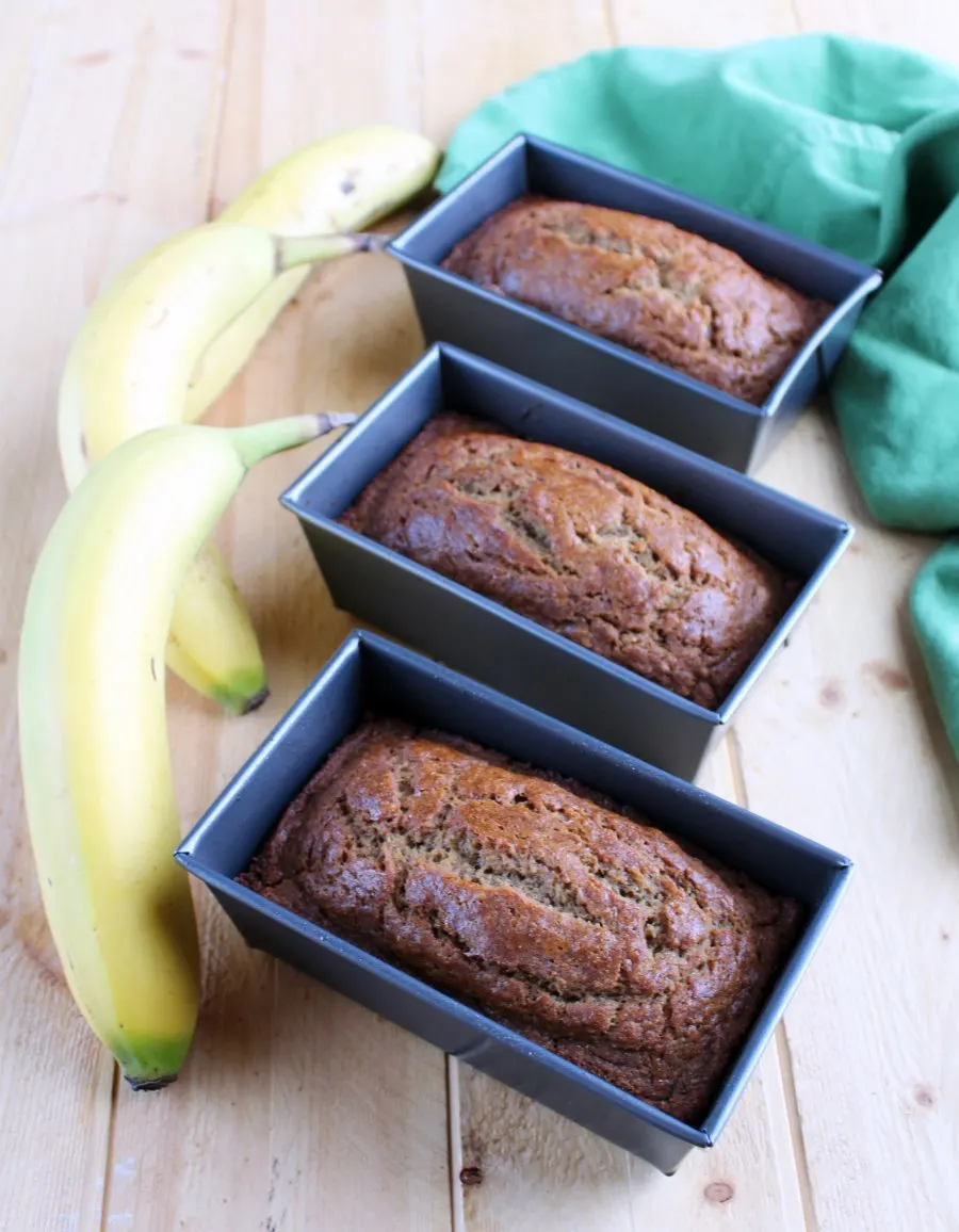 Mini loaf pans with freshly baked whole wheat banana bread next to a couple of fresh bananas.