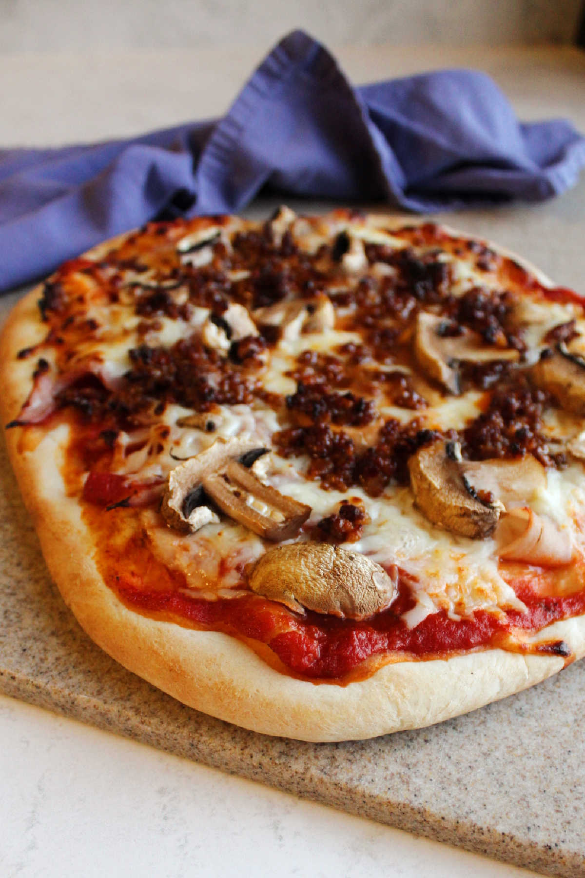 Cooked pizza with sourdough crust topped with sauce, cheese, mushrooms, sausage and ham.