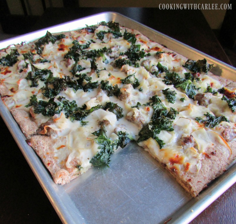 Sheet pan filled with pizza topped with kale, sausage and cheese.
