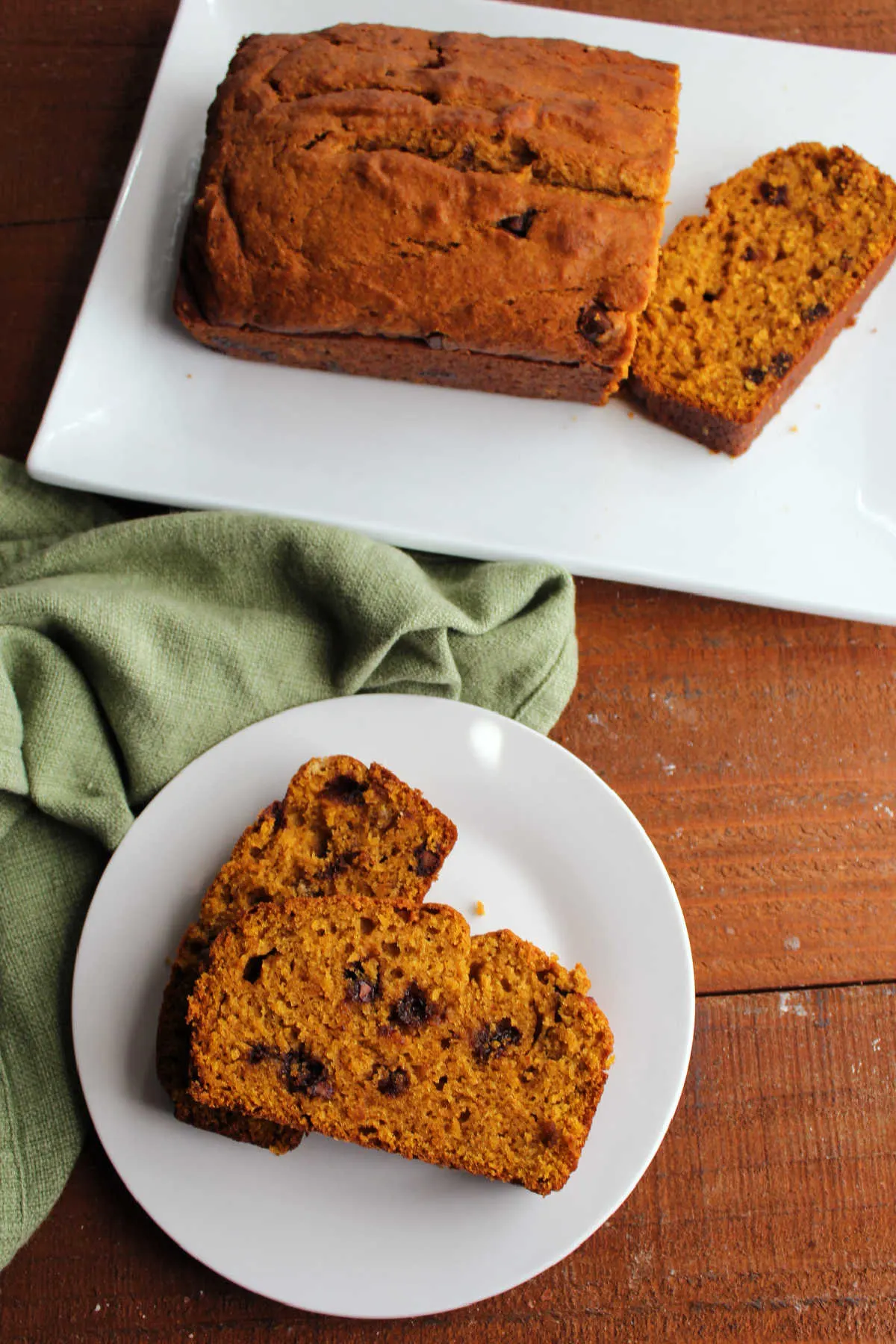 Slices of pumpkin chocolate chip bread on plate with remaining loaf on platter in the background.