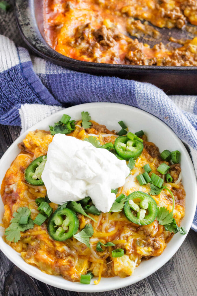 Plate of tamale pie topped with sliced jalapenos and a big dollop of sour cream.