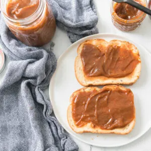 pumpkin butter spread over two slices of toast next to jar of homemade pumpkin butter.