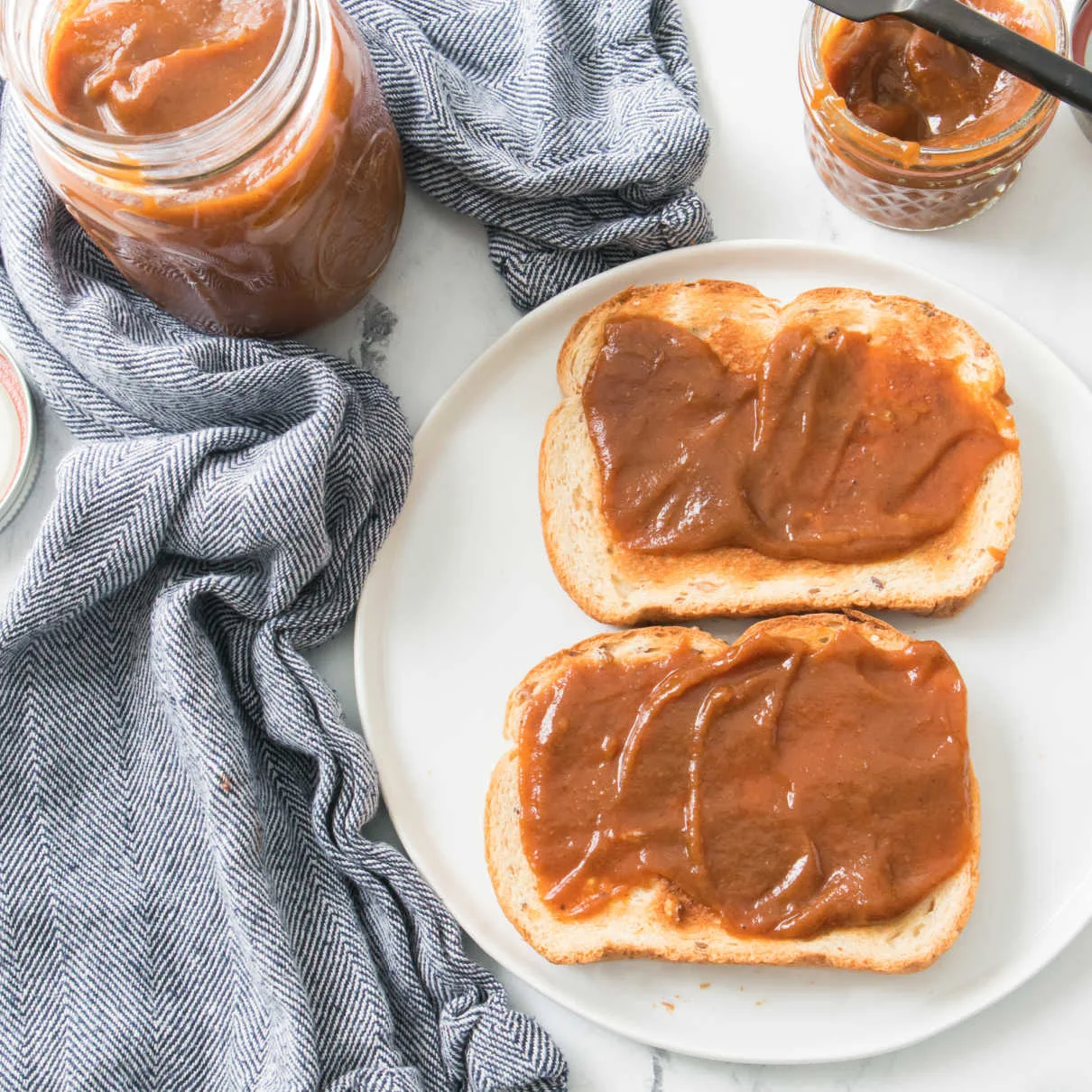 pumpkin butter spread over two slices of toast next to jar of homemade pumpkin butter.