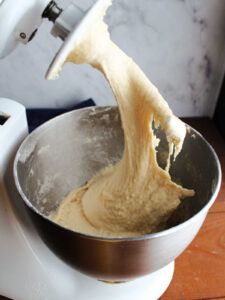 Lifting dough hook out of mixer bowl showing slack dough inside.