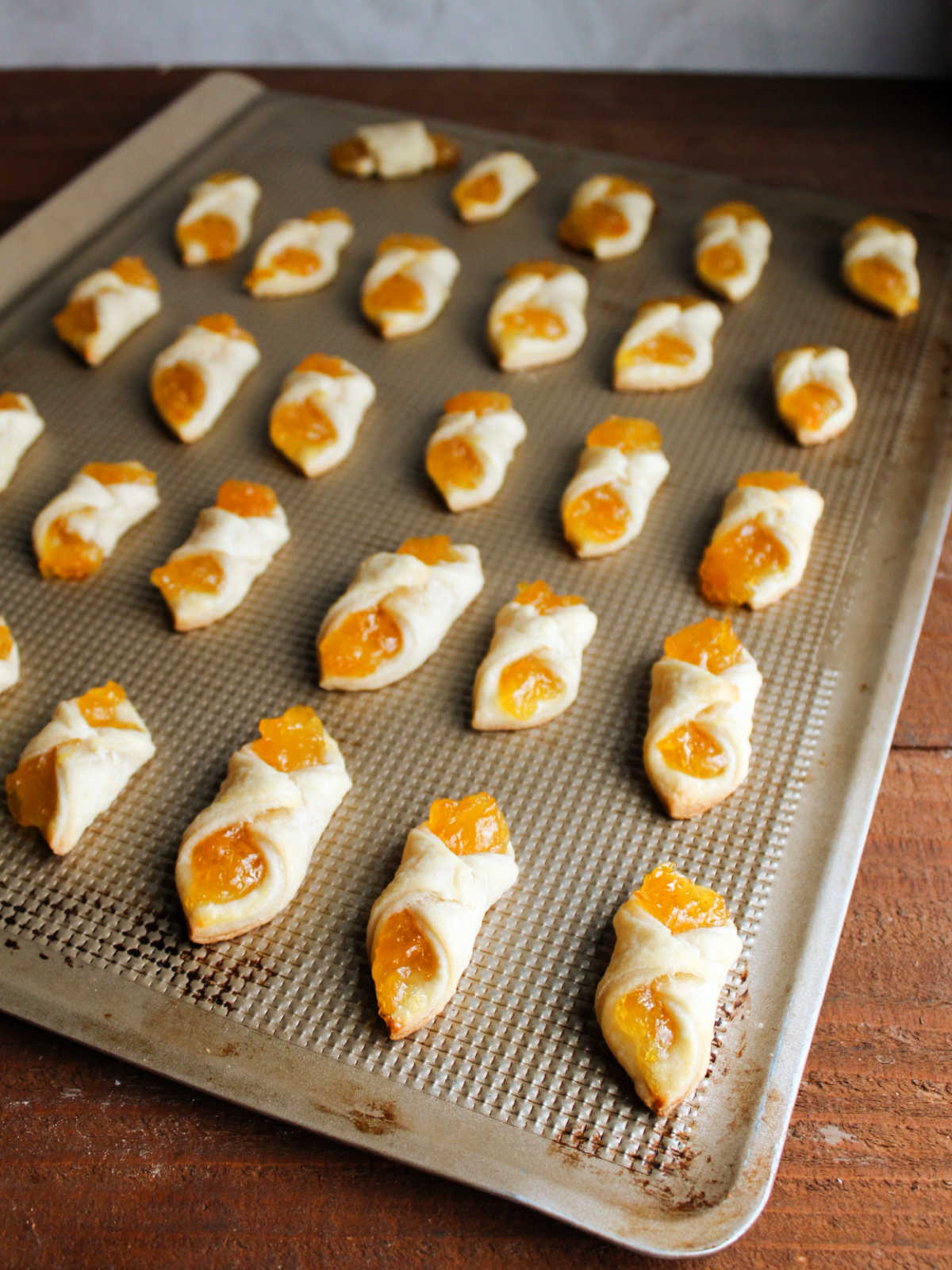 Cookie tray of freshly baked apricot kolacky cookies showing how the pastry puffed up and the filling set.