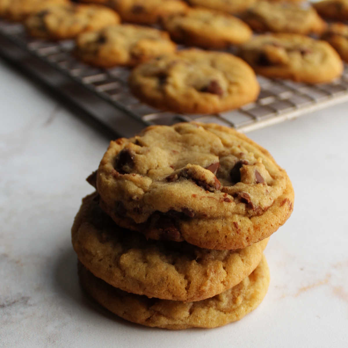 Stack of chocolate chip cookies in front of cooling rack of cookies.