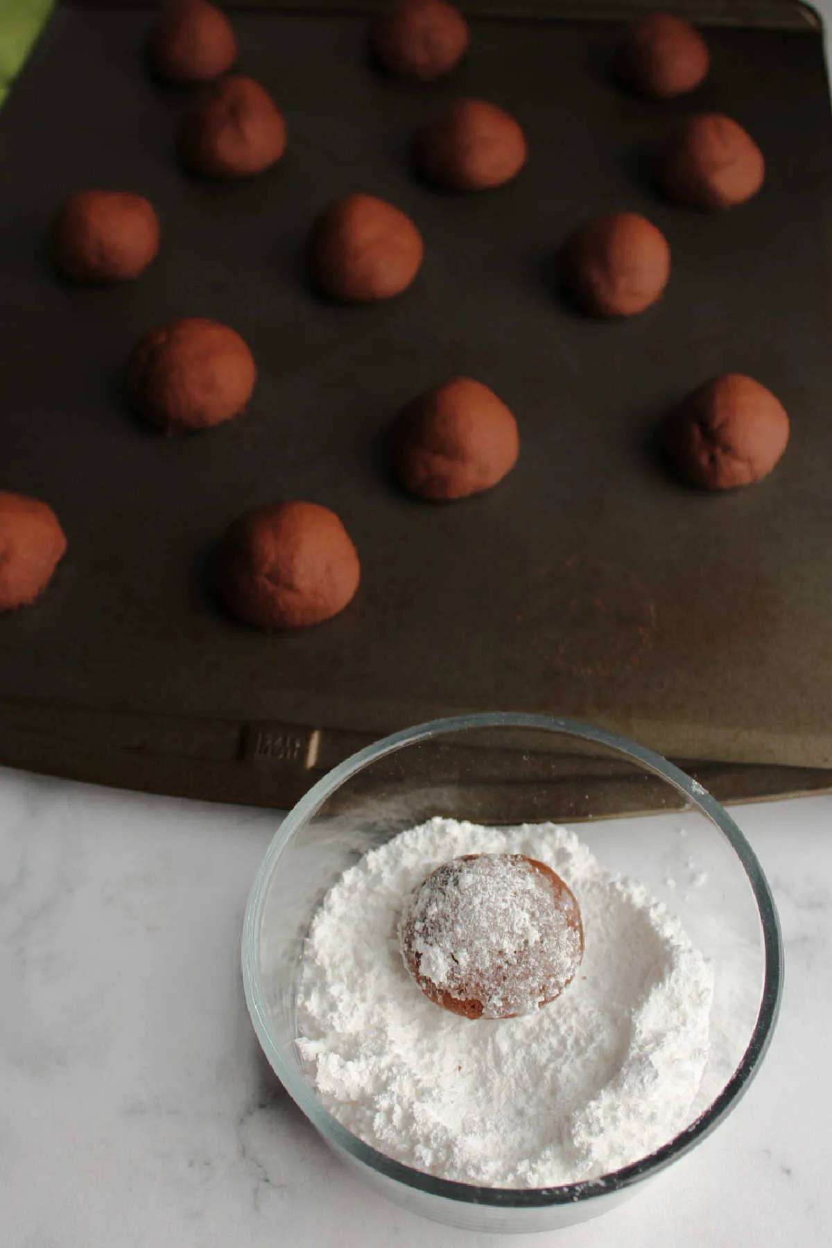 Rolling baked chocolate cookies in a bowl of powdered sugar.
