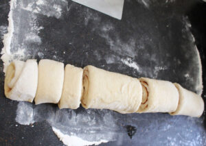 Cutting log of cinnamon roll dough into 12 equal pieces.