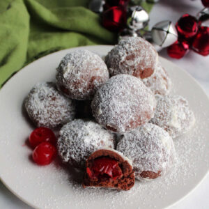 Chocolate covered cherry snowball cookies with powdered sugar on the outside and a maraschino cherry on the inside.