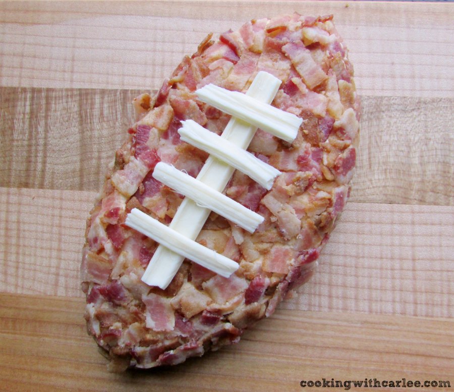 bacon covered cheese ball in the shape of a football with cheese laces