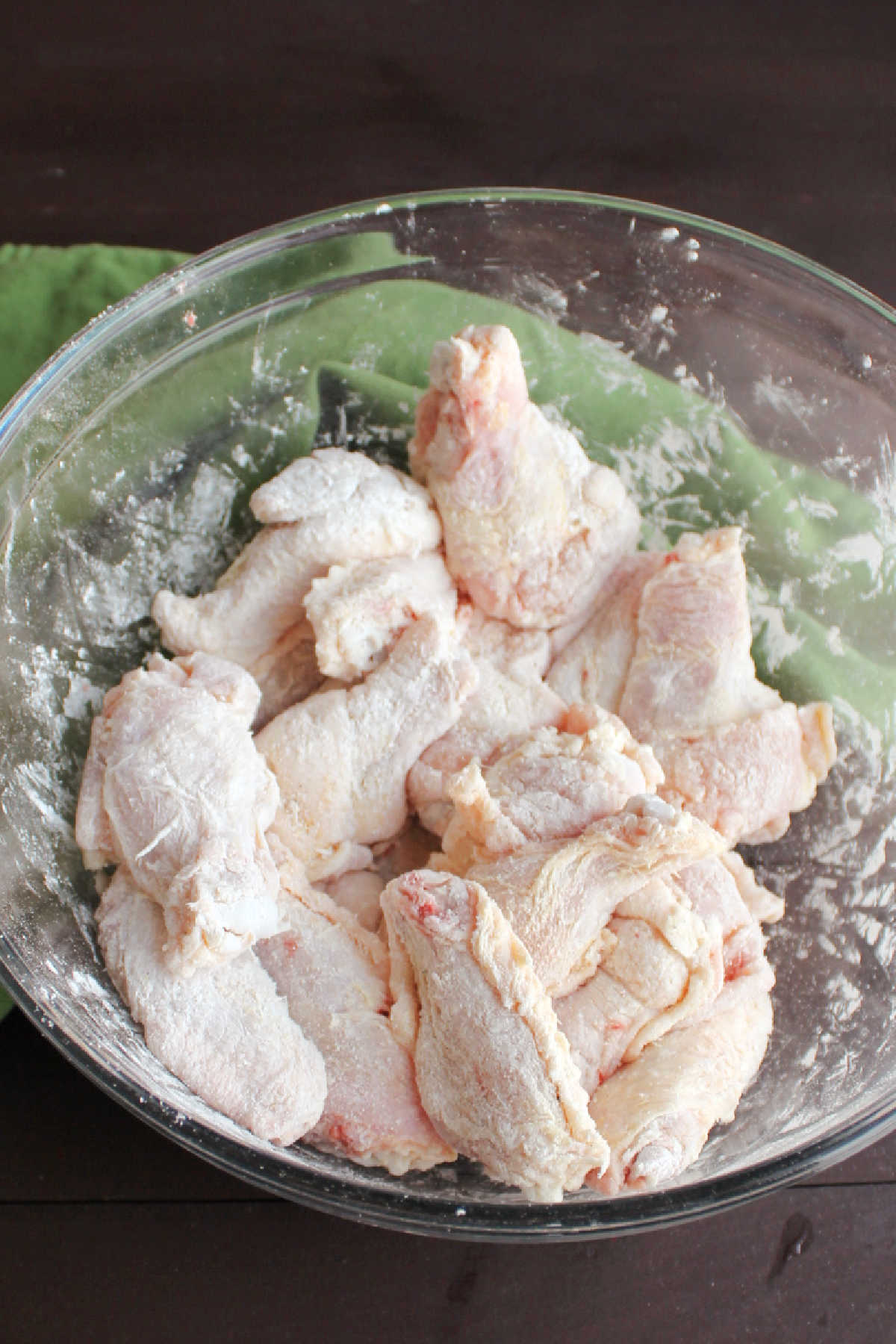 Wing pieces getting coated in spices, corn starch and baking soda in mixing bowl.