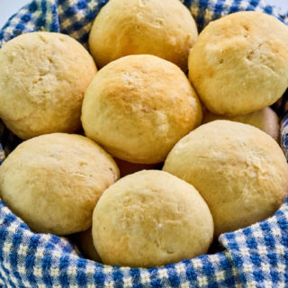 Basket lined with blue and white checked towel and filled with soft golden brown potato rolls.
