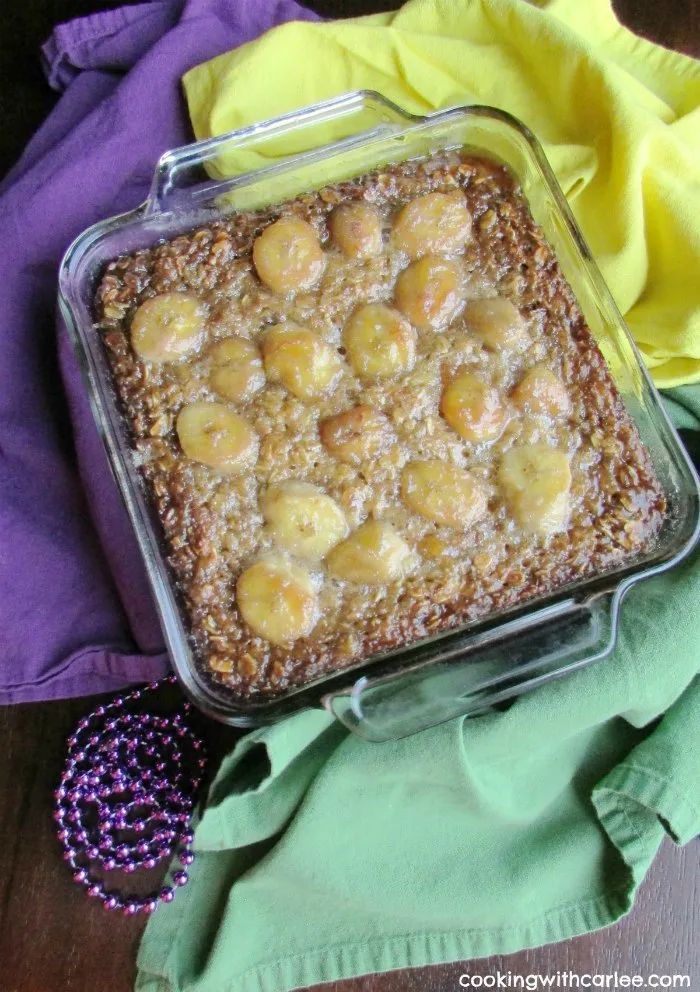 square baking dish filled with baked oatmeal with a layer of bananas foster inspired topping with beads and Mardis Gras colors around it.