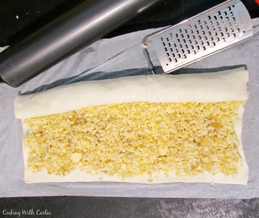 puff pastry topped with golden onions and shredded cheese next to microplane.
