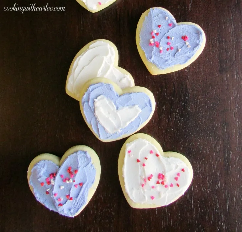Sour cream cookies cut in the shape of hearts topped with buttercream frosting and sprinkles.
