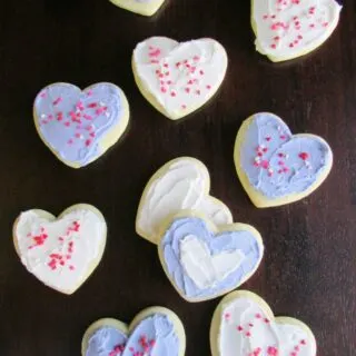 heart shaped sour cream cookies with white and lavender buttercream and sprinkles on top.