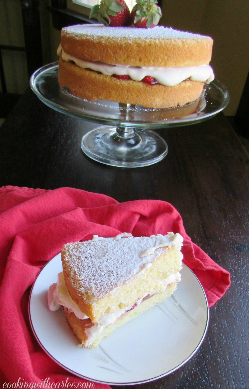 Slice of Victoria sponge on plate with remaining cake in background, strawberry and chantilly cream filling showing.