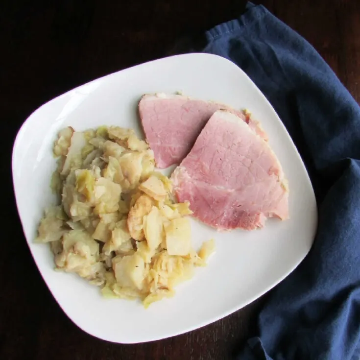 Plate with slices of ham and a big serving of sauteed cabbage with potatoes and Parmesan cheese.