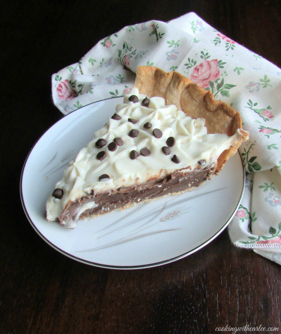 slice of pie on plate with creamy chocolate pudding and whipped cream piped on top with mini chocolate chips for garnish. 