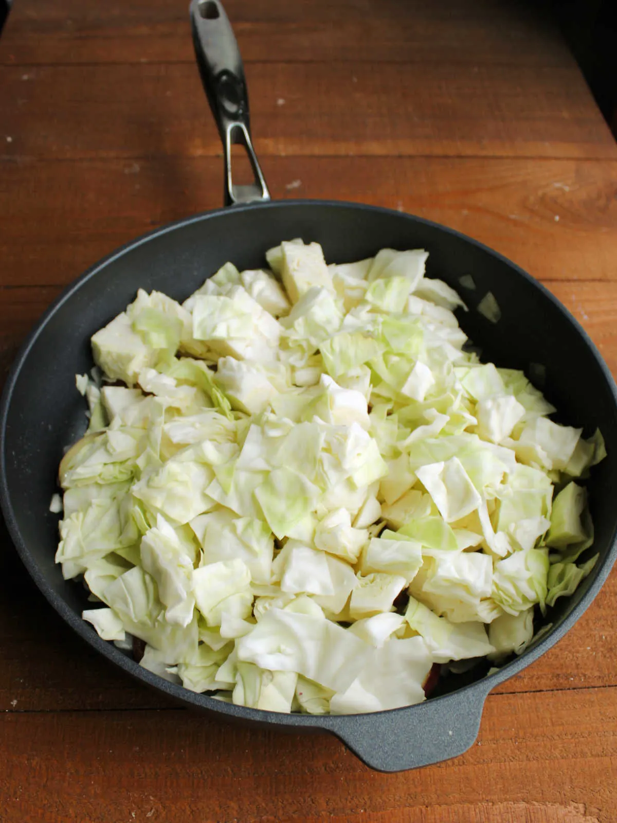 Adding chopped cabbage to skillet with partially cooked potatoes and onions.