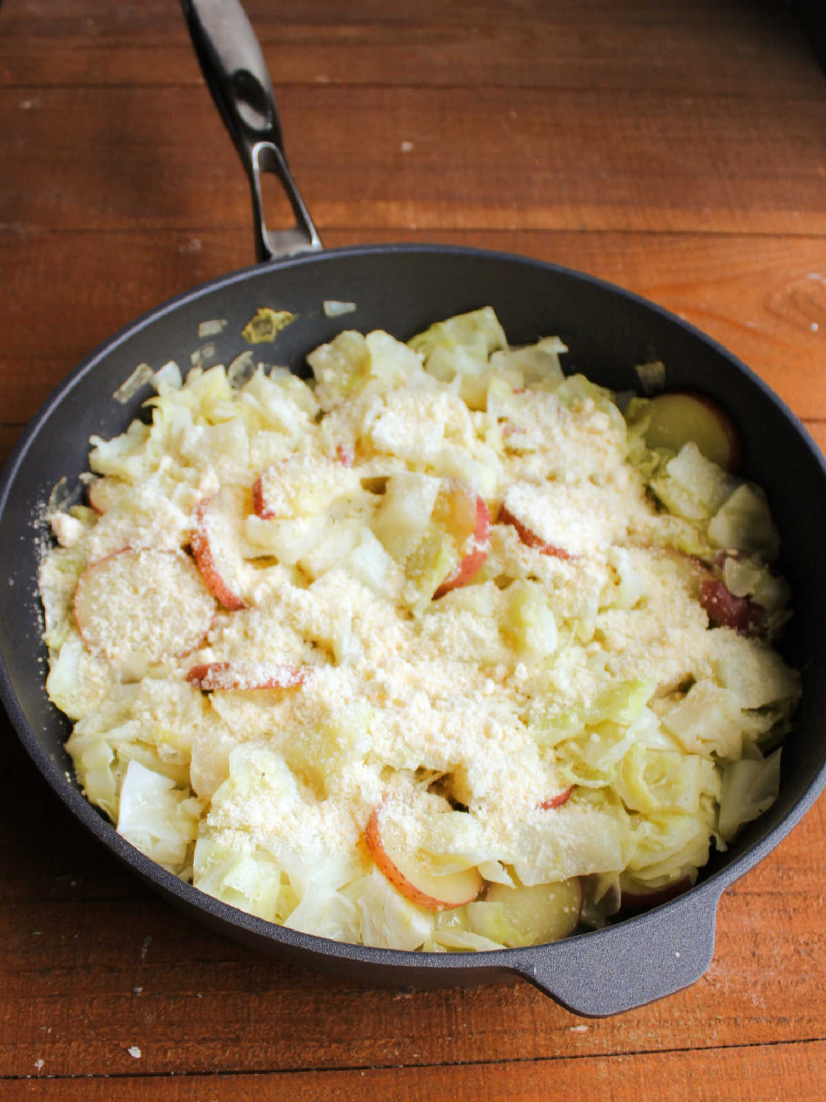 Skillet filled with cooked cabbage and potatoes topped with grated Parmesan cheese.